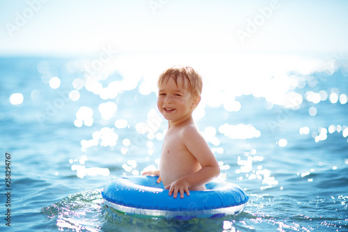 three years old boy playing at the beach with swimming ring