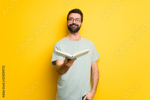 Man with beard and green shirt holding a book and giving it to someone