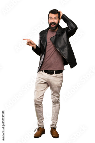 Handsome man with beard surprised and pointing finger to the side over isolated white background © luismolinero