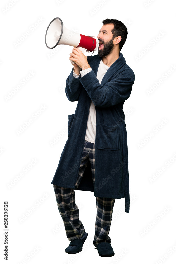 Man with beard in pajamas shouting through a megaphone over isolated white background Man with beard in pajamas shouting through a megaphone over isolated white background