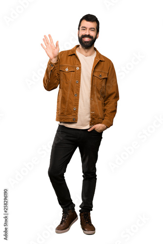 Handsome man with beard saluting with hand with happy expression over isolated white background