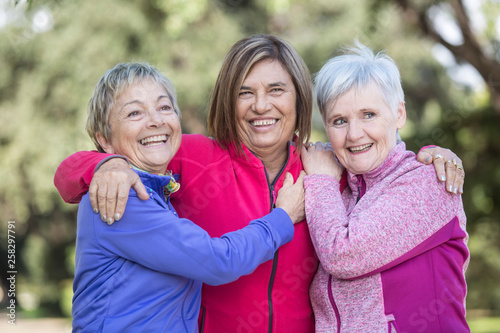 trio di  di amiche mature ridono felici vestite con tute colorate al parco photo