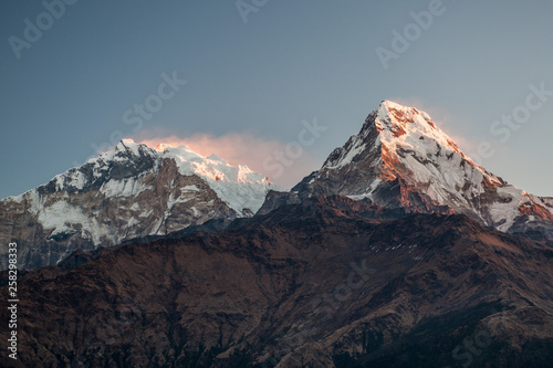 Poonhill view of Annapurnas. Warm pink and orange sunrise light over Annapurna mountain range with beautiful clouds, view from Poon hill in Himalayas, Nepal. Annapurna one and Annapurna south.
