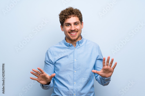 Blonde man over blue wall smiling