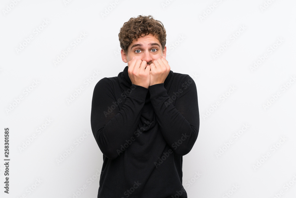 Blonde man over isolated white wall nervous and scared putting hands to mouth Blonde man over isolated white wall nervous and scared putting hands to mouth