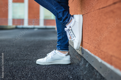Tableau sur toile Woman with leather white sneaker leaning wall in city, close-up side view