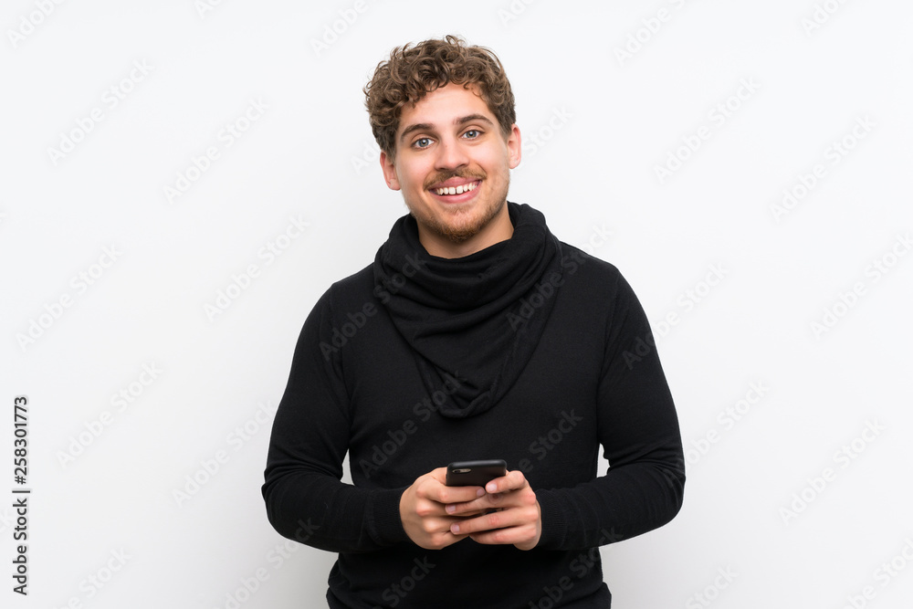 Blonde man over isolated white wall sending a message with the mobile Blonde man over isolated white wall sending a message with the mobile
