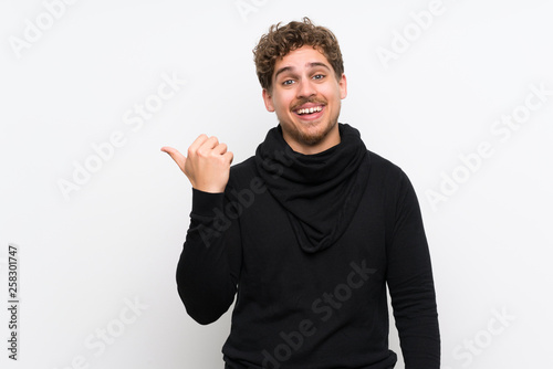 Blonde man over isolated white wall pointing to the side to present a product