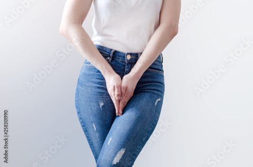 Young woman in jeans standing with her hands between legs photo