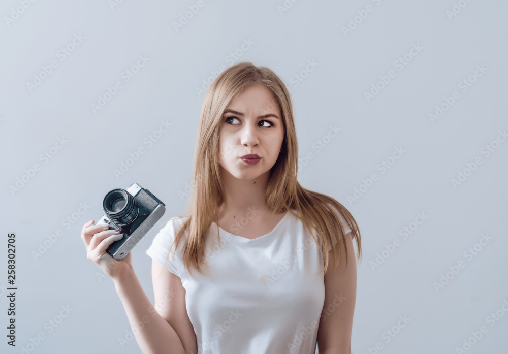 Fototapeta premium Attractive girl holding a vintage camera in her hands. Confusedly looks