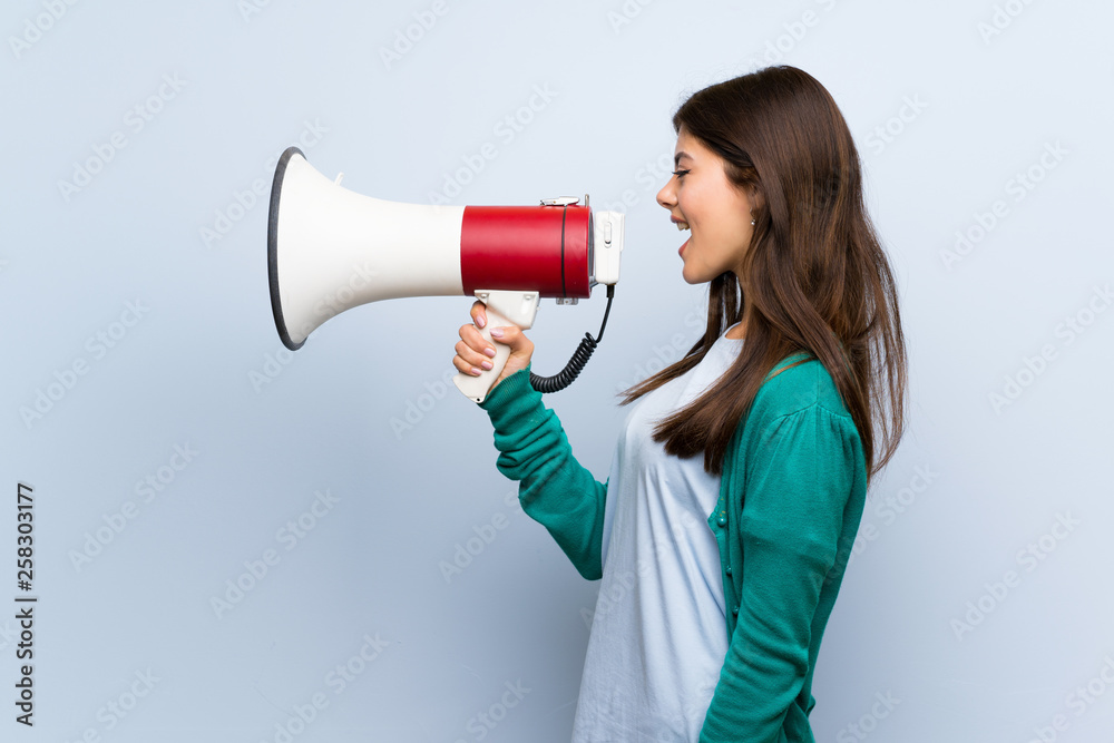Teenager girl over blue wall shouting through a megaphone Teenager girl over blue wall shouting through a megaphone