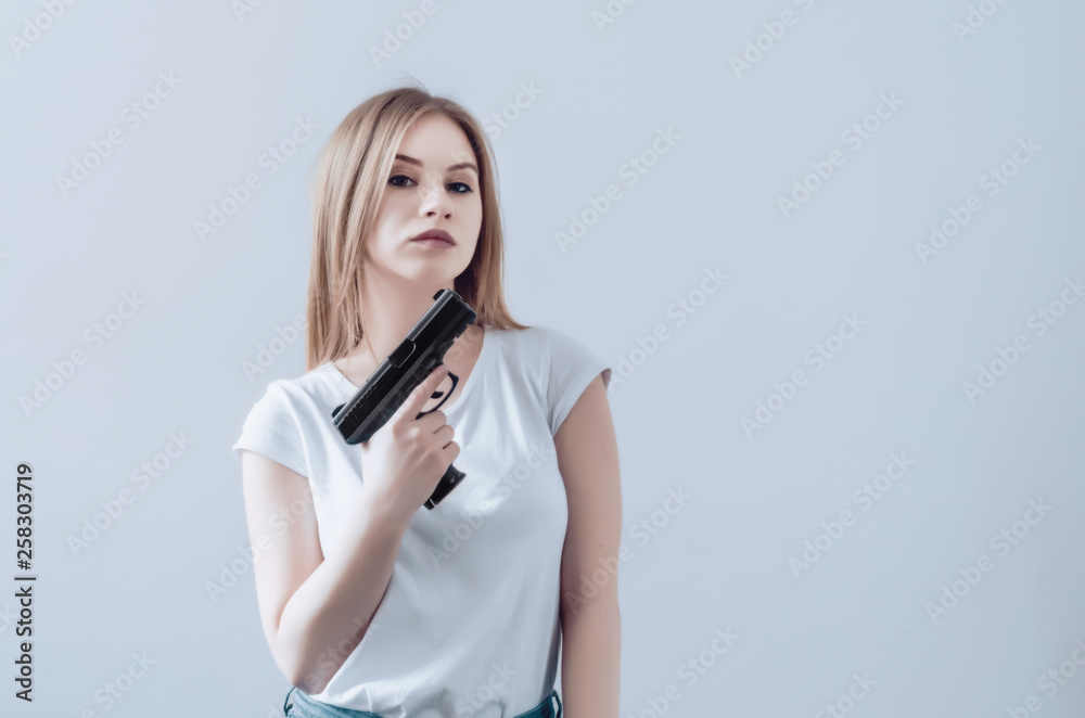 Young beautiful girl holding a gun in her hands. Pistol raised up to face. Young beautiful girl holding a gun in her hands. Pistol raised up to face.