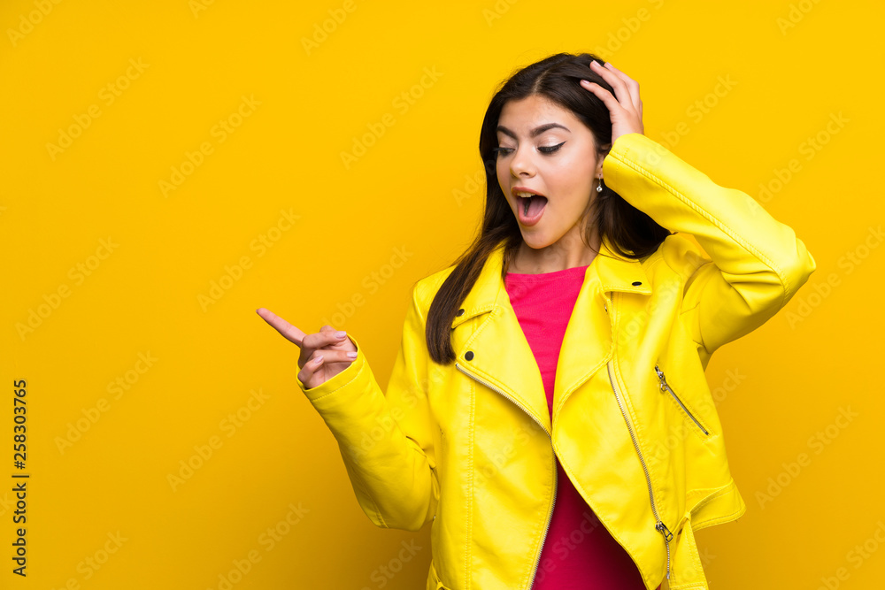Teenager girl over yellow wall pointing finger to the side and presenting a product Teenager girl over yellow wall pointing finger to the side and presenting a product