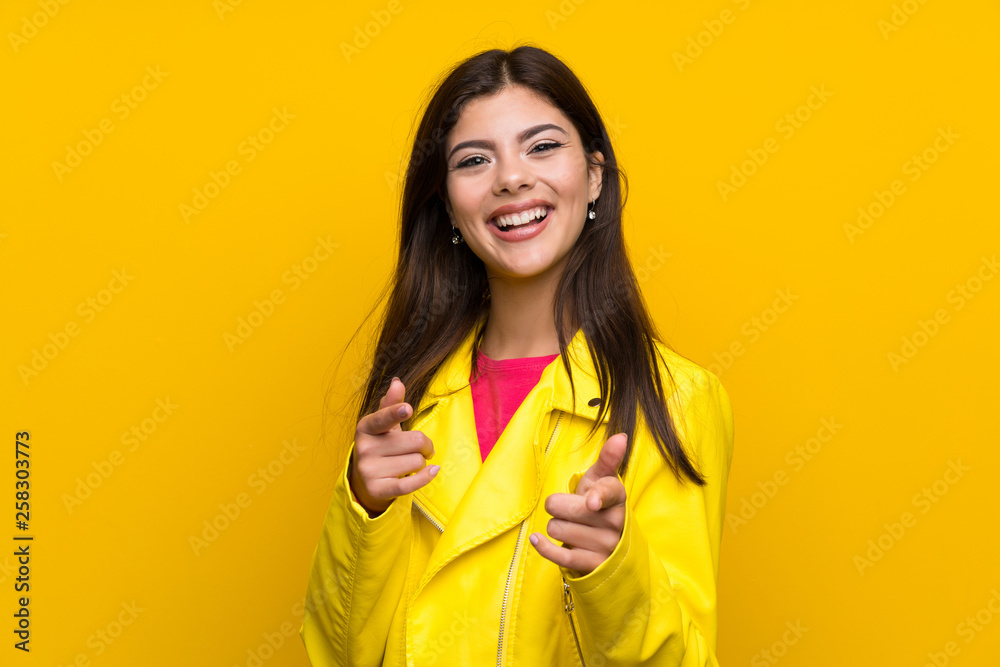 Teenager girl over yellow wall points finger at you