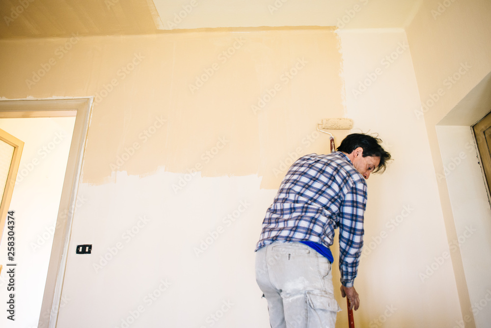 husband father of forty years, paints house wall - man painting wall of a room-man performs DIY painting at home