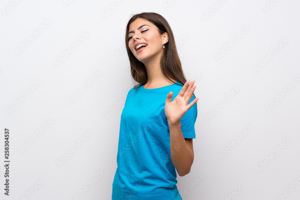 Teenager girl with blue shirt saluting with hand with happy expression