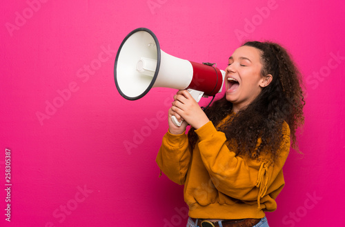 Teenager girl over pink wall shouting through a megaphone
