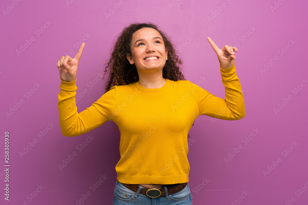 Teenager girl over purple wall surprised and pointing up