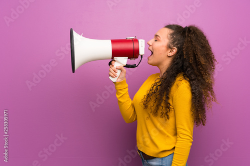 Teenager girl over purple wall shouting through a megaphone
