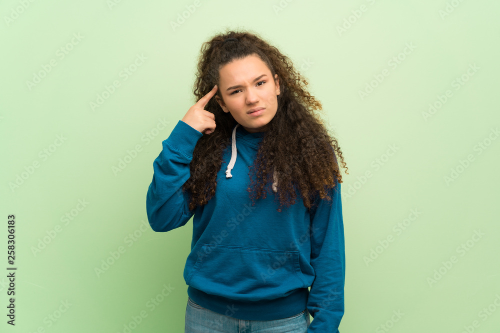 Teenager girl over green wall making the gesture of madness putting finger on the head