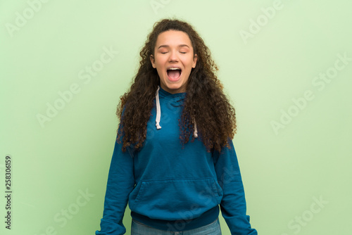 Teenager girl over green wall shouting to the front with mouth wide open