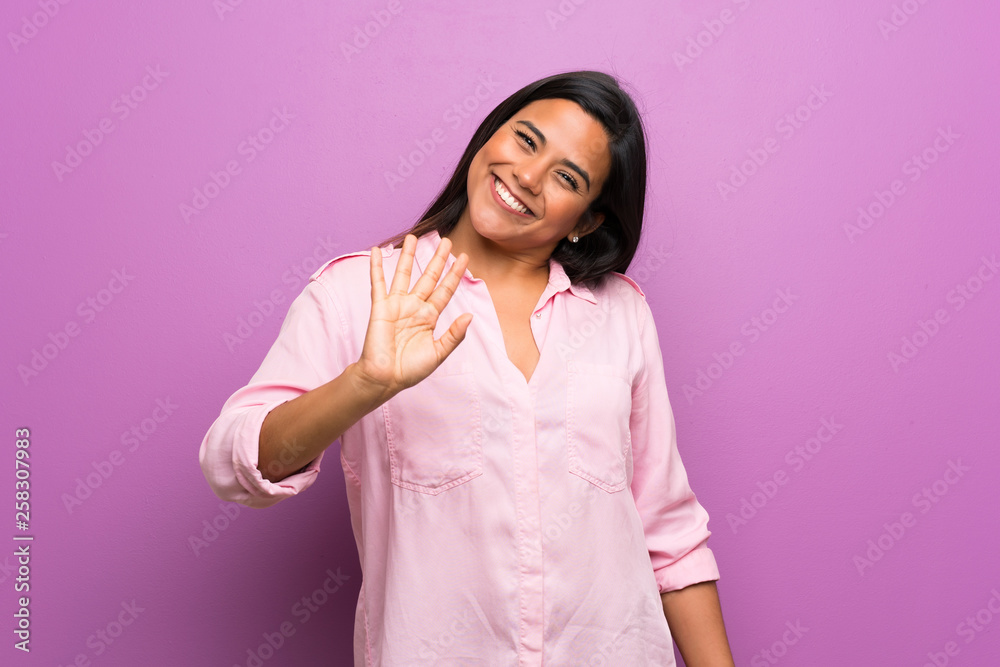Young Colombian girl over purple wall saluting with hand with happy expression Young Colombian girl over purple wall saluting with hand with happy expression