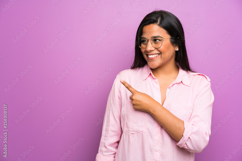 Fototapeta premium Young Colombian girl over purple wall pointing finger to the side