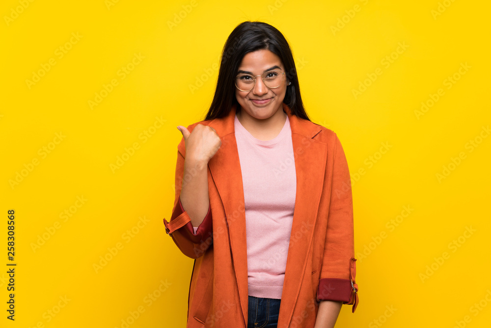 Young Colombian girl over yellow wall pointing to the side to present a product Young Colombian girl over yellow wall pointing to the side to present a product