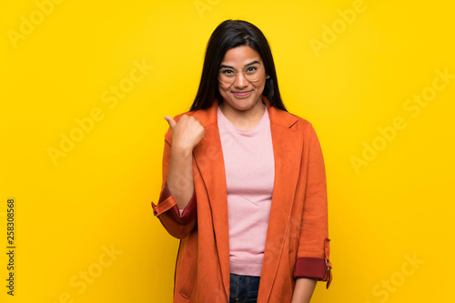Young Colombian girl over yellow wall pointing to the side to present a product