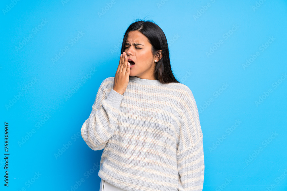 Young Colombian girl with sweater yawning and covering wide open mouth with hand Young Colombian girl with sweater yawning and covering wide open mouth with hand