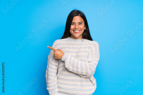 Young Colombian girl with sweater pointing to the side to present a product
