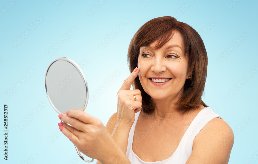 beauty and old people concept - portrait of smiling senior woman with mirror touching her face over blue background beauty and old people concept - portrait of smiling senior woman with mirror touching her face over blue background
