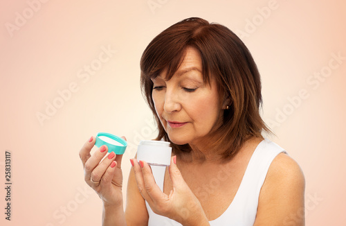 beauty, skincare and cosmetics concept - senior woman with cream jar over beige background
