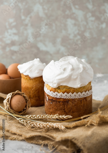 Two traditionally baked orthodox paskas with glace icing and bright blue and violet flowers on white woooden background with lace fabric. Easter cakes. Selective focus, copy space photo
