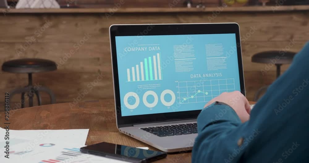 Man sits at a coffee shop table and looks at the company data graphs and diagrams. Analyzing the company progress and predictions.