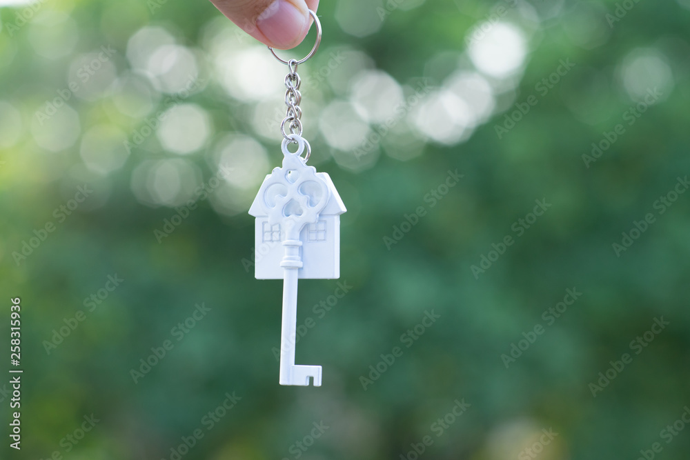 Hanging home key with house keyring with green garden background Hanging home key with house keyring with green garden background
