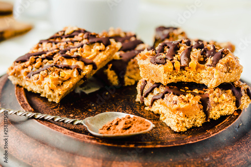 Granola bar cake with date caramel and chocolate. Healthy sweet dessert snack. Cereal granola bar with nuts, fruit and berries on a clay dark plate. Close-up.
