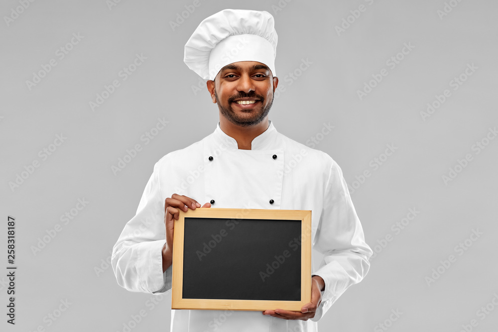 cooking, profession and people concept - happy male indian chef in toque with blank chalkboard for menu over grey background cooking, profession and people concept - happy male indian chef in toque with blank chalkboard for menu over grey background