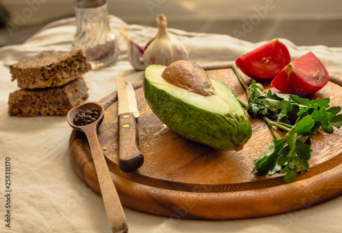 Ingredients for guacamole on a wooden board. Parsley, avocado, tomatoes, garlic, black pepper.