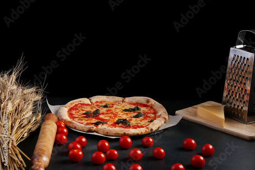 izza margarita with tomatoes and ingredients on dark stone background with copy space photo