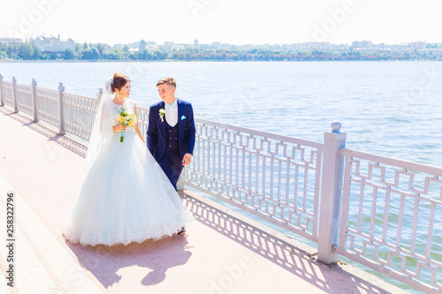 the newlyweds hold hands and walk near the lake. The bride holdi photo