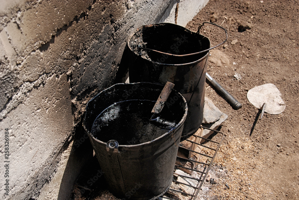 Dirty buckets with tar are on the grill on the ground at the construction site Dirty buckets with tar are on the grill on the ground at the construction site