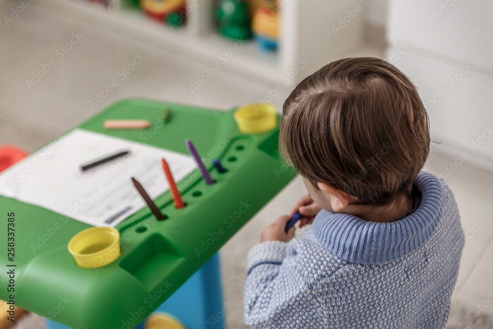 A little blond boy with a pacifier and dressed in blue, paints with crayons on a sheet, while he is in his bedroom A little blond boy with a pacifier and dressed in blue, paints with crayons on a sheet, while he is in his bedroom
