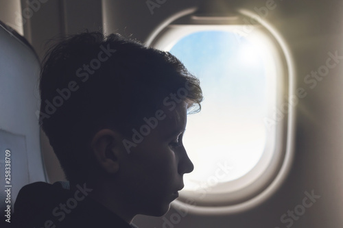 A boy have flight sitting the airplane window or porthole.