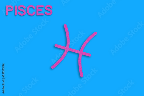 Symbol of astrological sign and word pisces cut out of purple paper on blue table. Top view. Horoscope concept