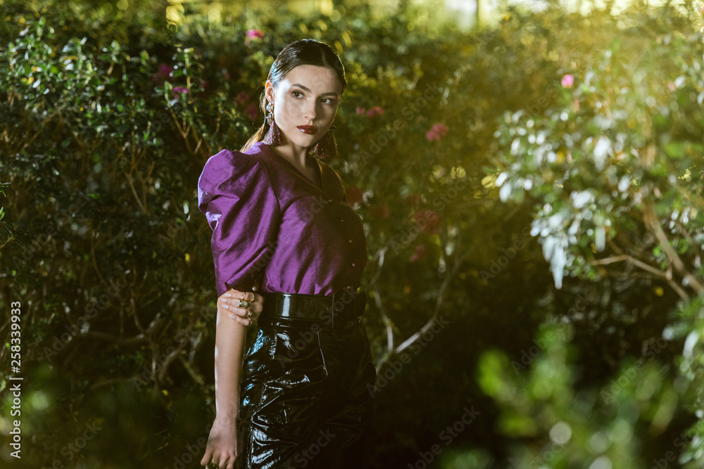 Pensive girl in purple blouse and leather pants posing in botanical garden Pensive girl in purple blouse and leather pants posing in botanical garden