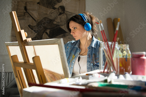 Young woman with retro headphones painting on canvas