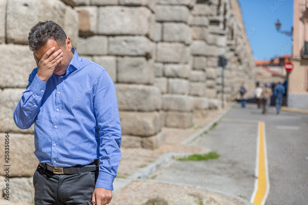 An elegant man in a blue shirt cries in the middle of the street because of a personal problem