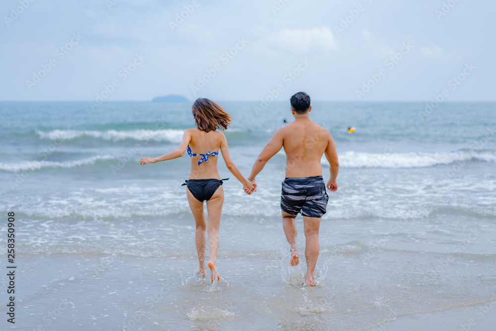 Young Asian honeymoon couple in holiday beach and walking on beach,They wear bikini and have a happy holiday.