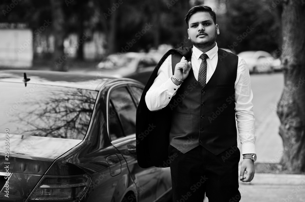 Stylish indian businessman in formal wear standing against black business car on street of city.